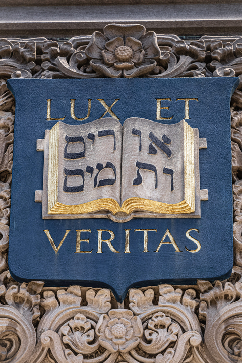 Close up of a stone carving of Yale's coat of arms features an open book and Yale's motto, Lux et Veritas